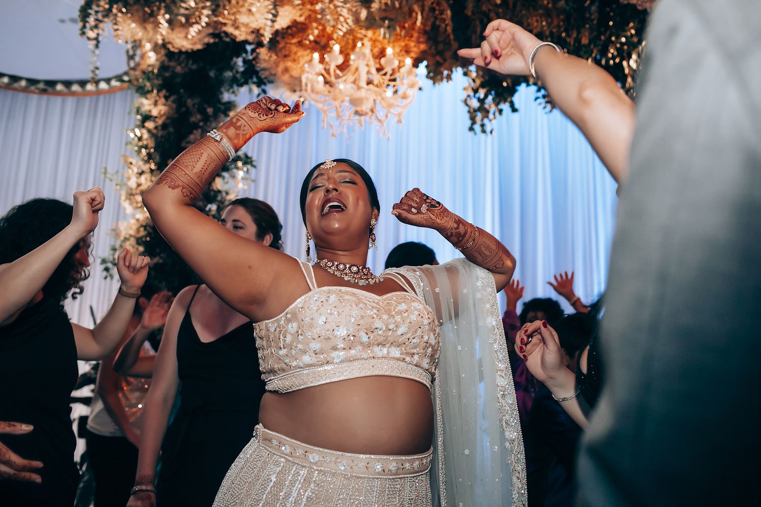 Joyful dancing celebration under floral decorations at Indian wedding reception.