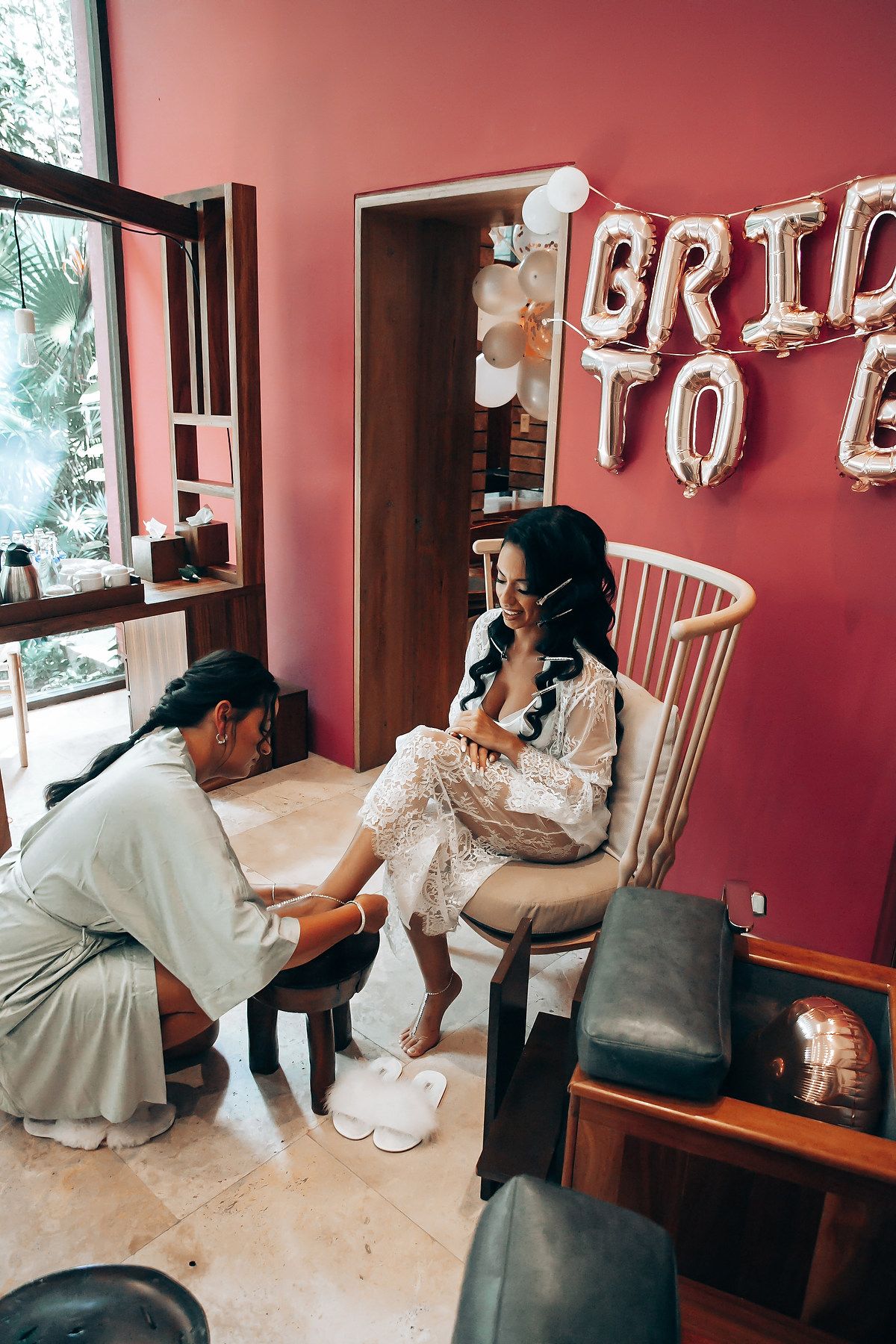 Wedding preparation scene showing someone helping with shoes in a room with burgundy walls.