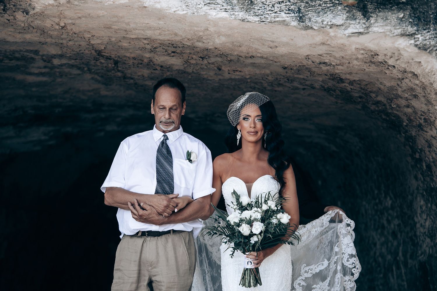 Wedding couple posing for a portrait in front of a dramatic cave entrance.