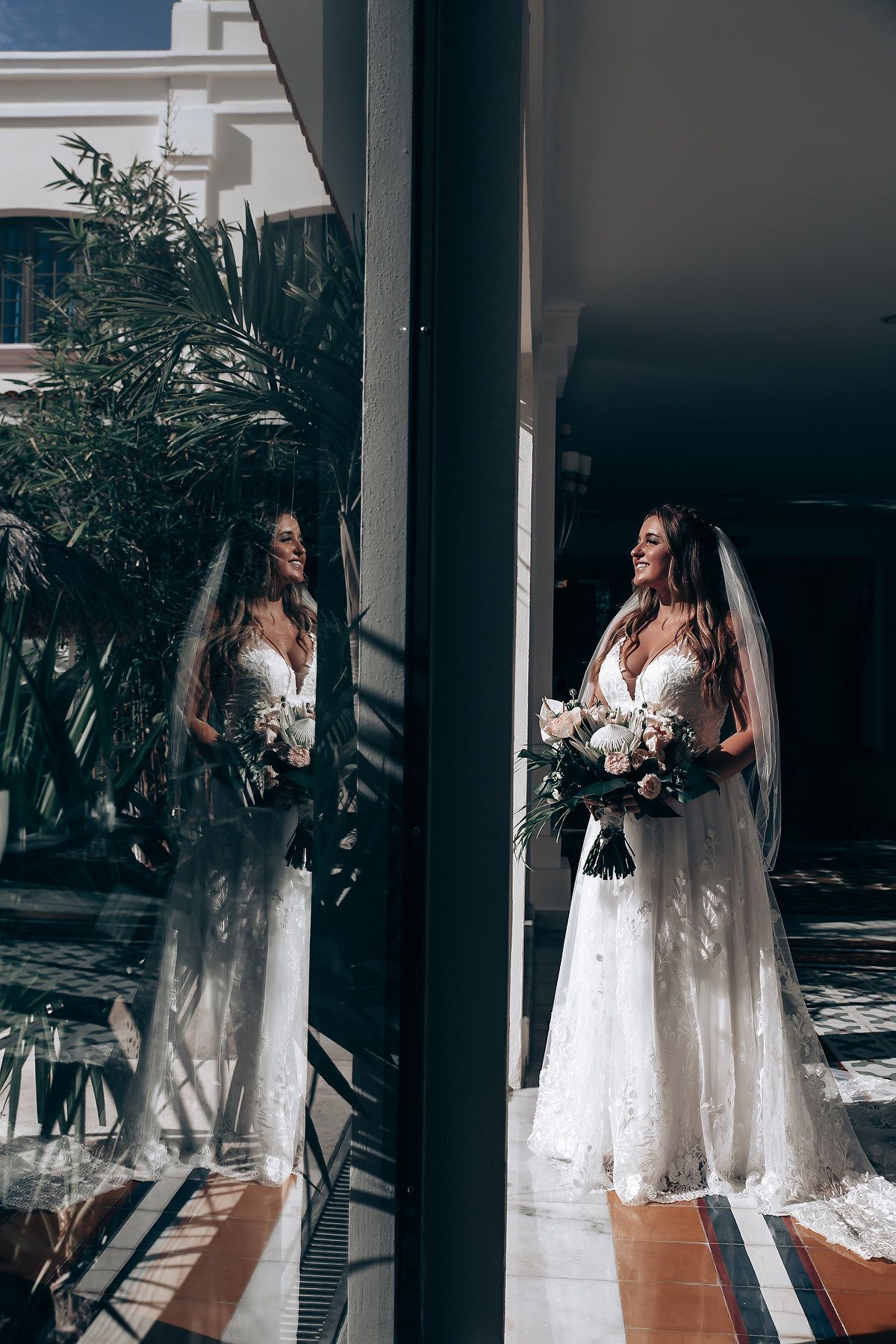 Bride in white wedding dress poses in architectural setting with dramatic lighting and shadows.