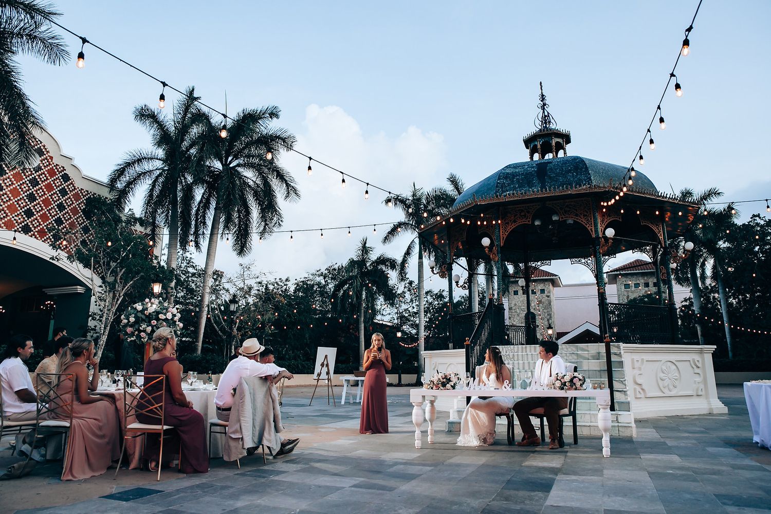 Panoramic view of wedding venue with palm trees and string lights at dusk.