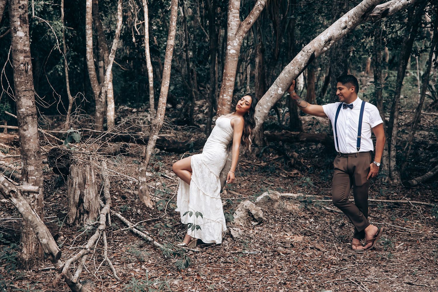 A couple embraces in a wooded setting with natural light filtering through the trees.