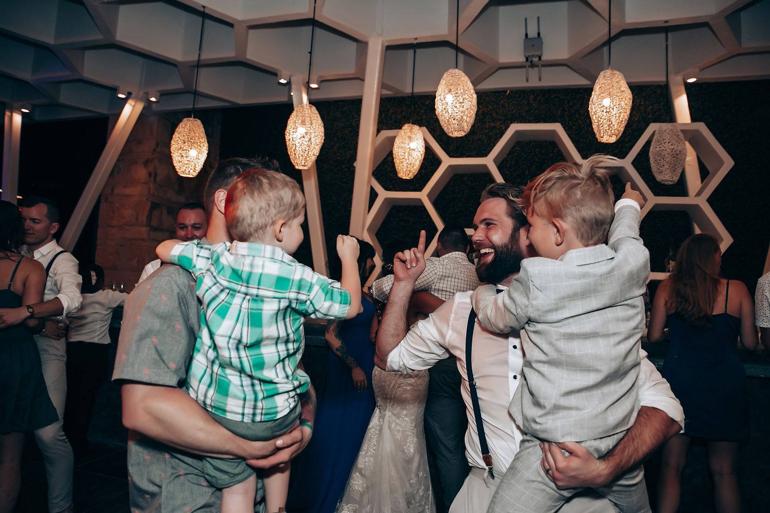 Couples dancing together under geometric ceiling patterns at an evening wedding reception.