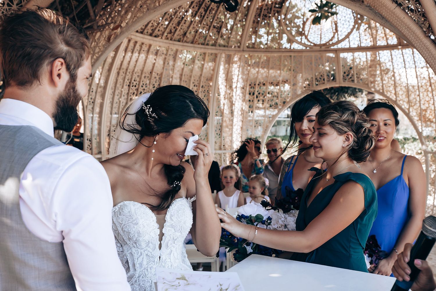 Wedding guests gather under a rustic wooden pergola during reception celebrations.