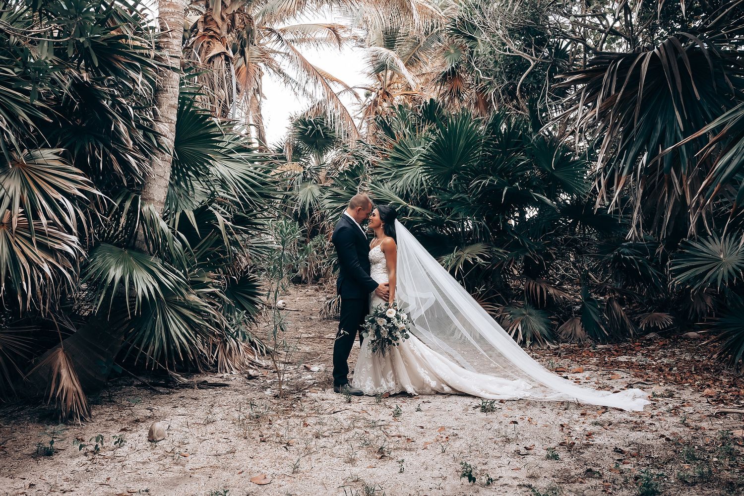 Wedding ceremony in progress at tropical beach location with palm trees and natural decor.