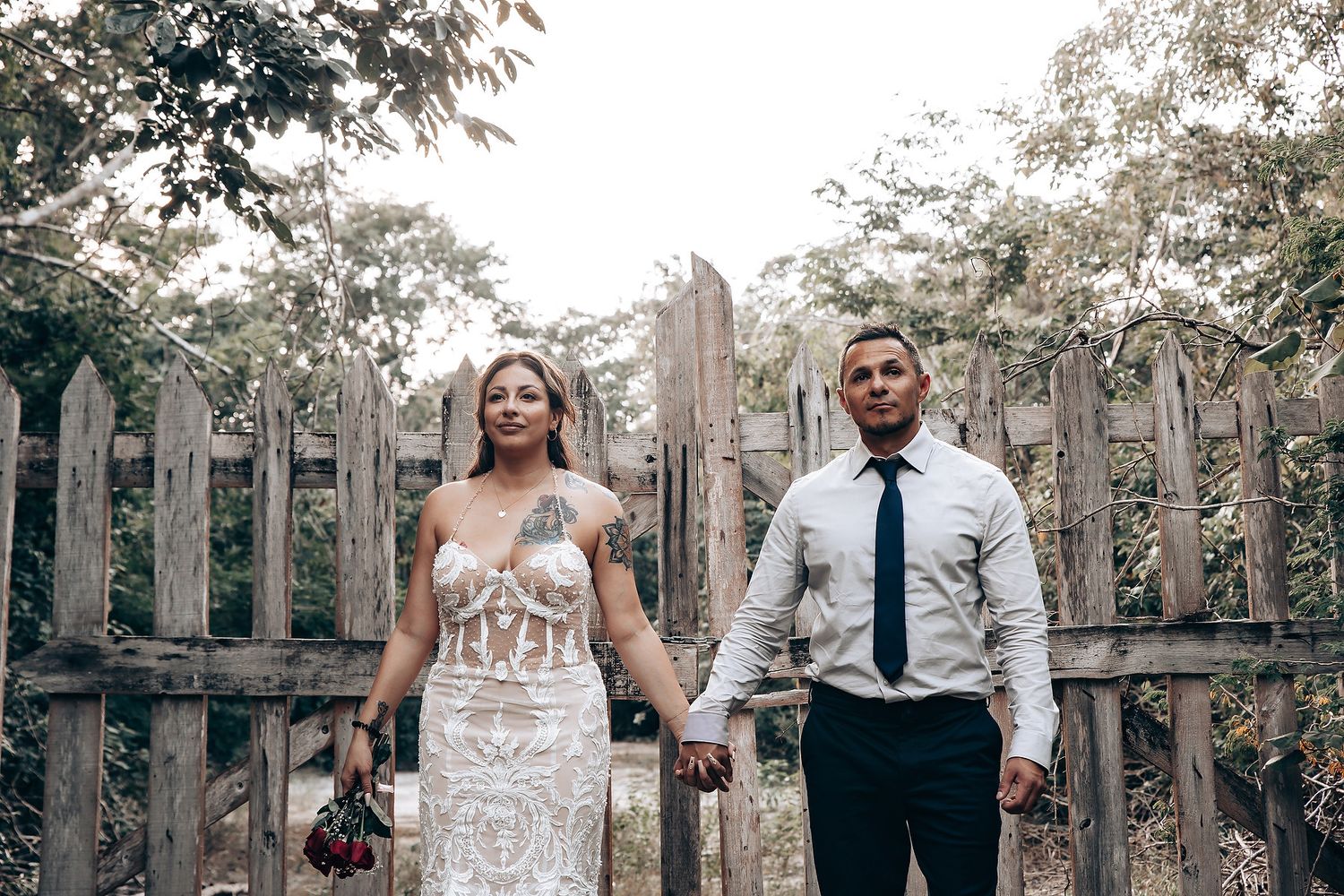 Wedding couple and guests standing in front of rustic wooden fence at outdoor venue.