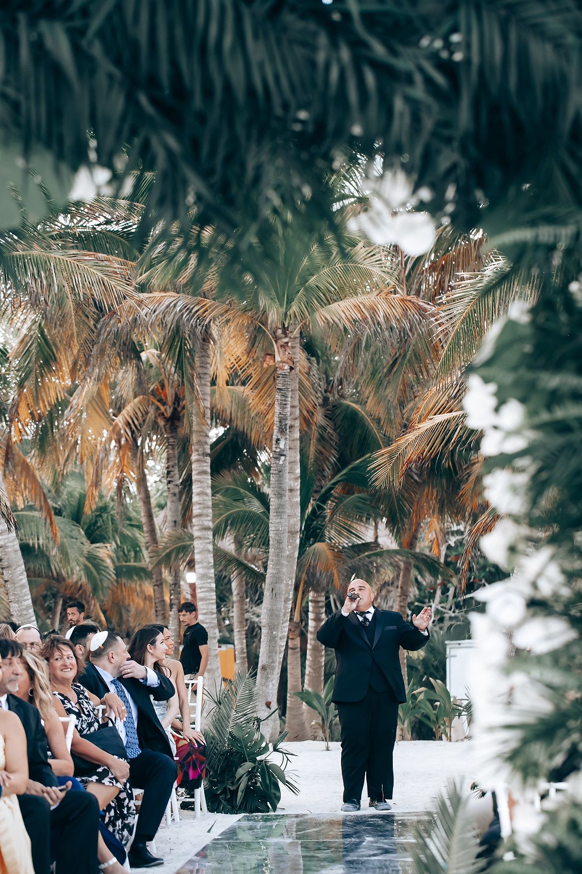 Tropical beach wedding ceremony setup with palm trees and rows of white chairs.