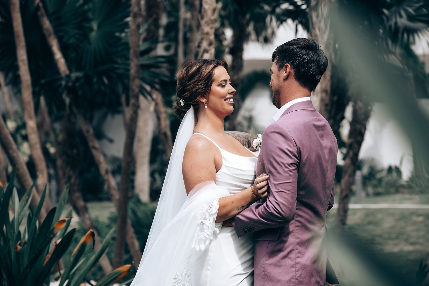 A couple embraces during a romantic beachside wedding ceremony surrounded by palm trees.