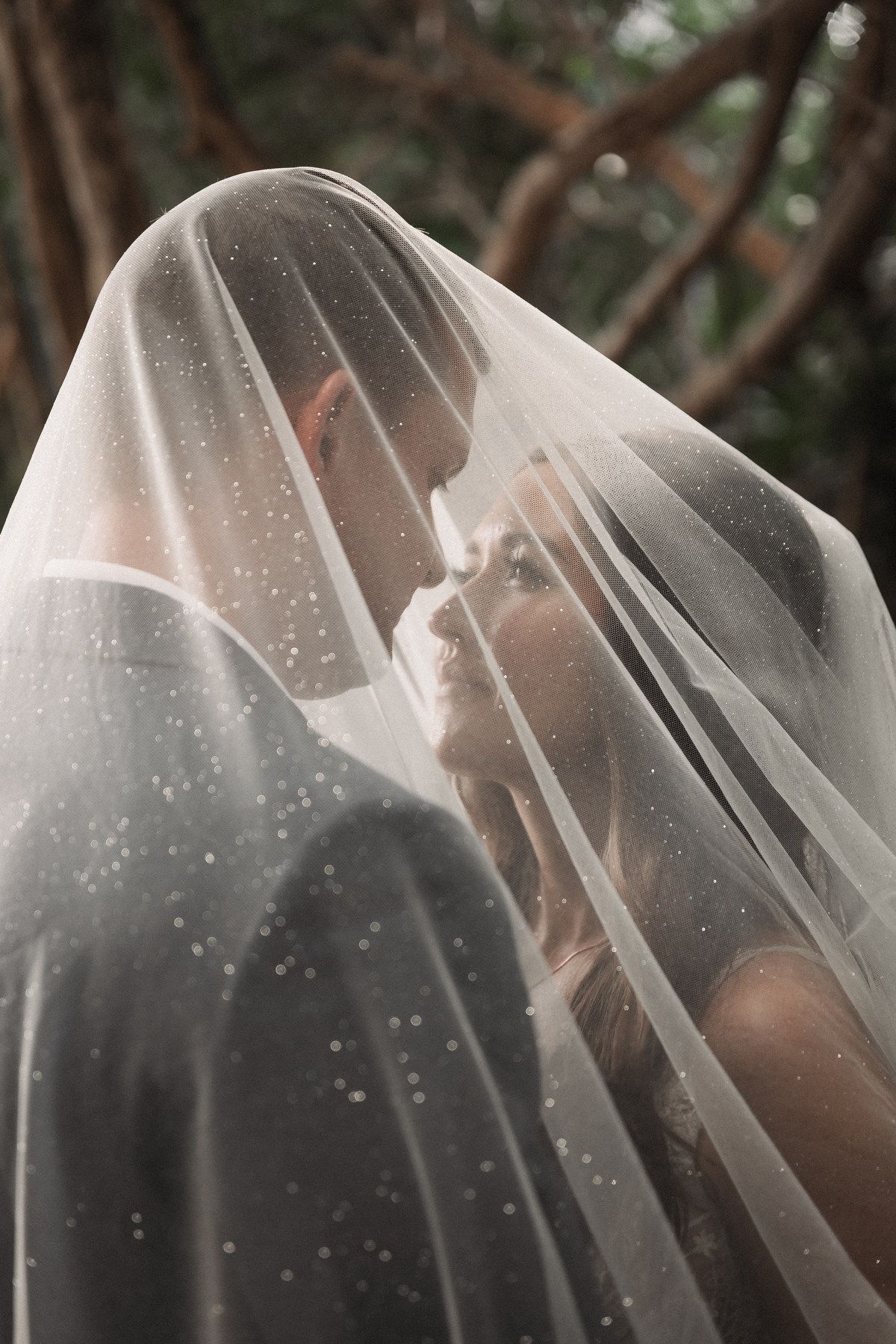 Romantic close-up of bride and groom sharing a kiss under a sparkled wedding veil outdoors.