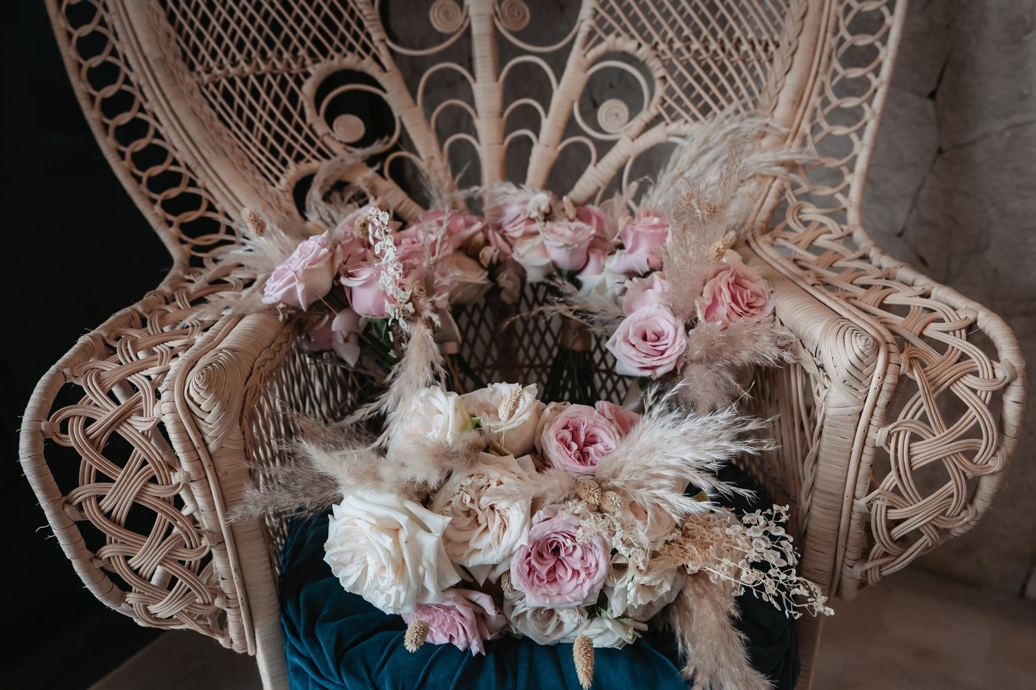 Elegant boho bridal bouquets with pink roses and pampas grass displayed on an ornate wicker peacock chair.