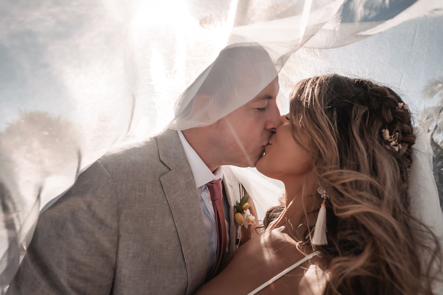 Intimate wedding couple sharing tender moment against bright sunlit background.