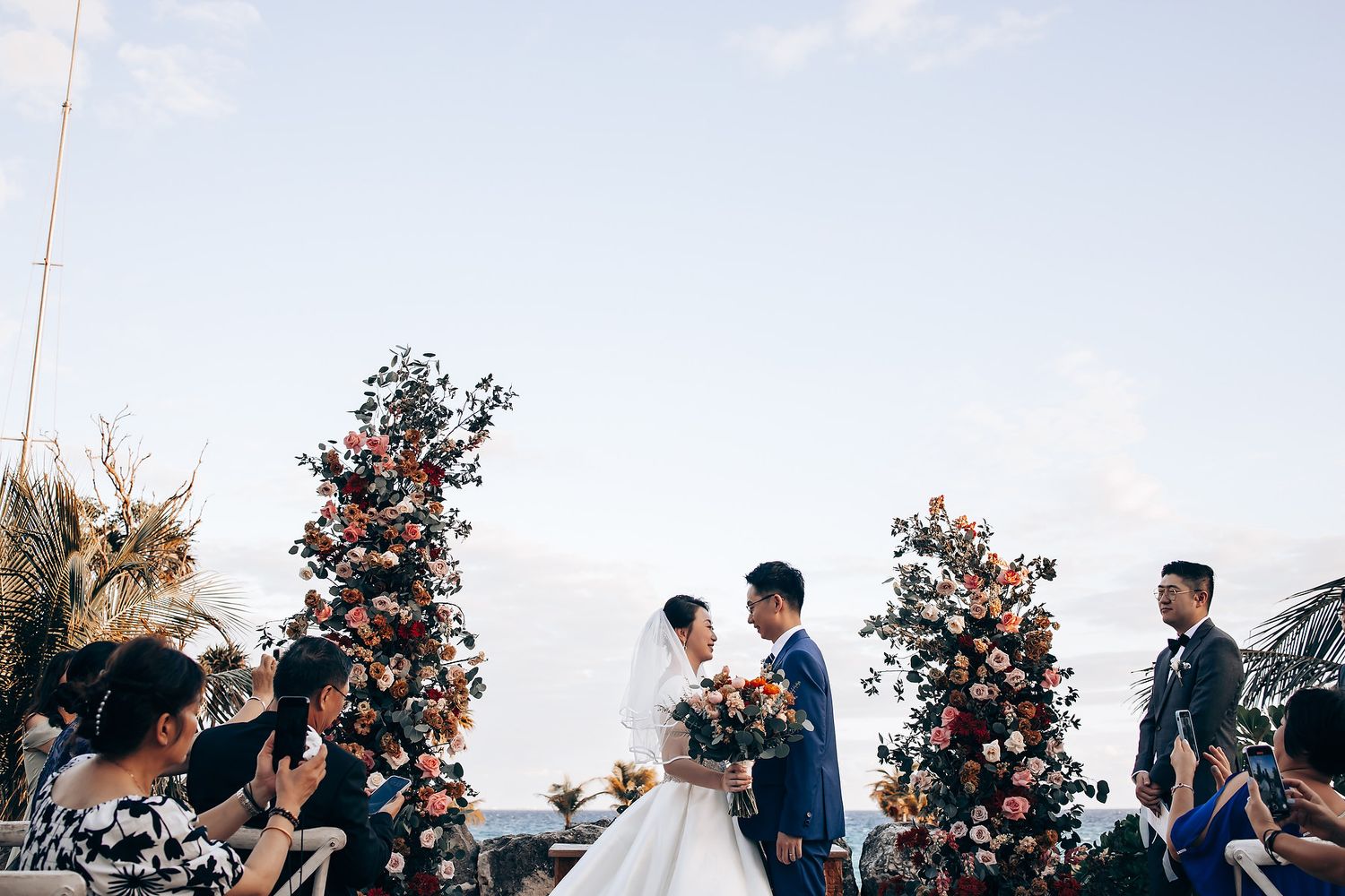 Wedding guests celebrating and cheering during an outdoor ceremony with floral arrangements.