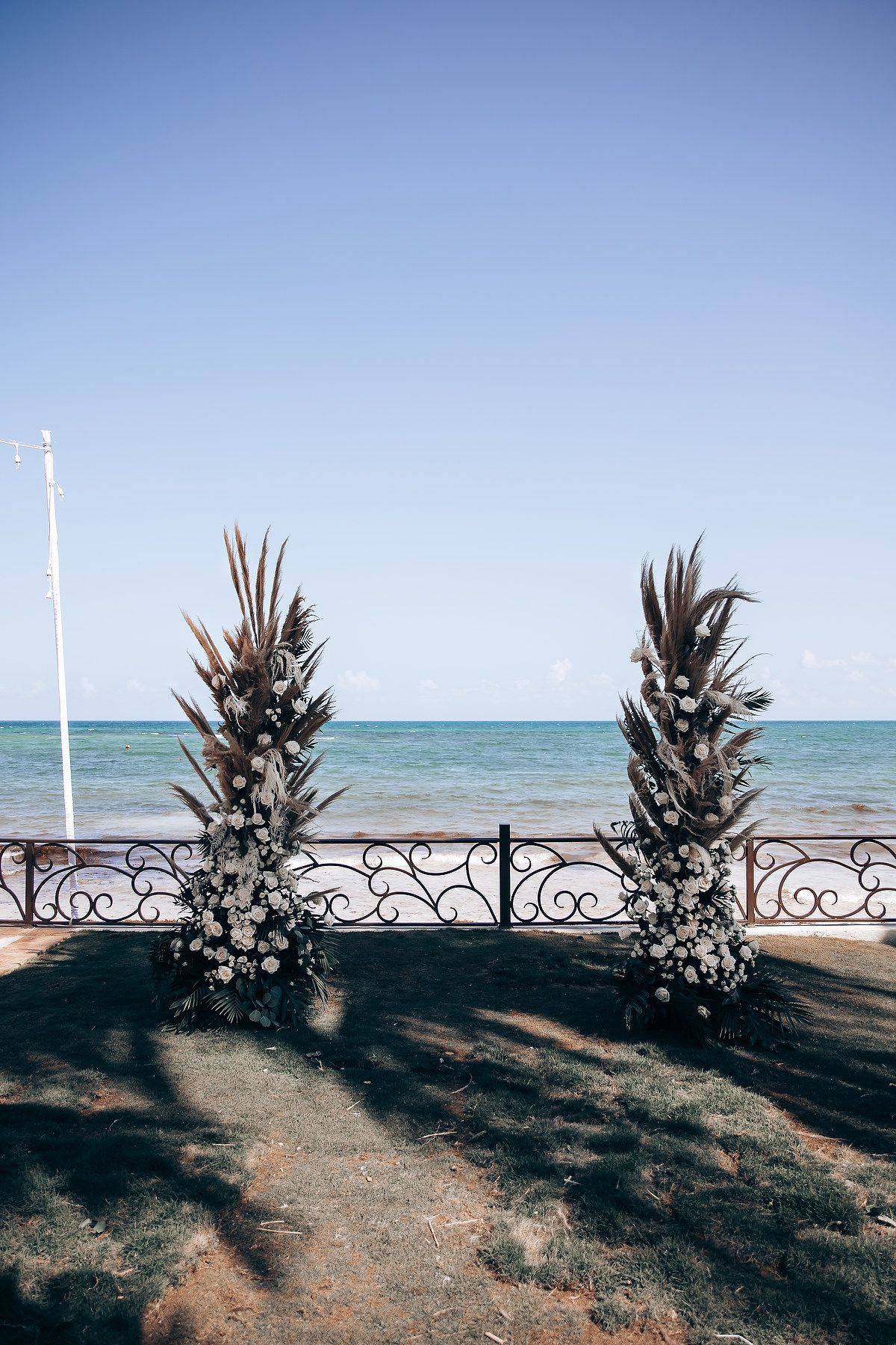 Tropical beach wedding ceremony setup with palm frond arrangements and white floral decorations.