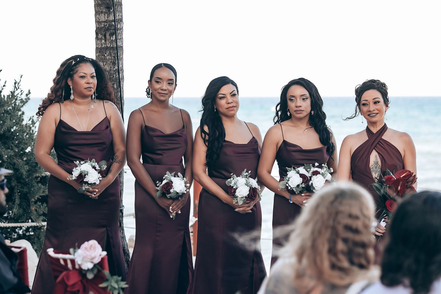Wedding party in burgundy dresses poses together on a tropical beach at sunset.