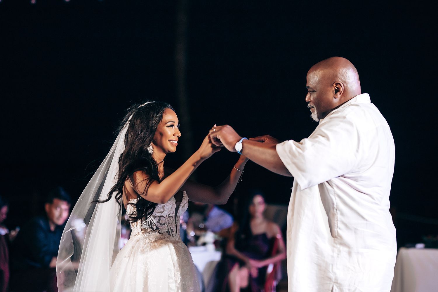 Romantic first dance moment at nighttime beach wedding reception with string lights overhead.