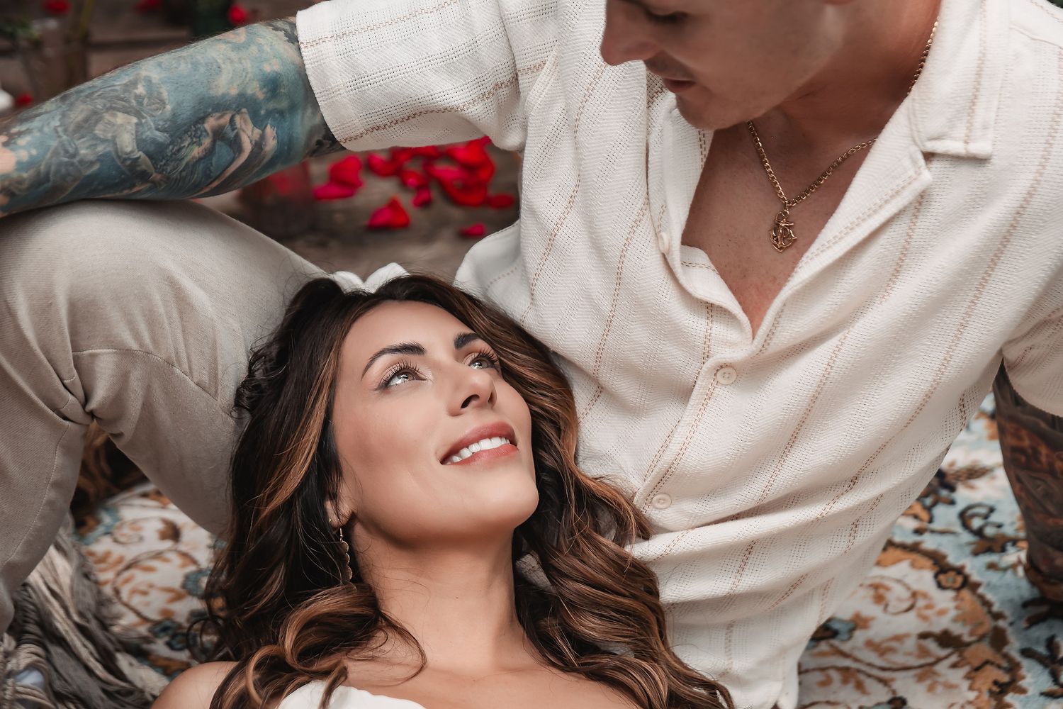 Romantic outdoor photoshoot with white outfits and scattered rose petals in a garden setting.