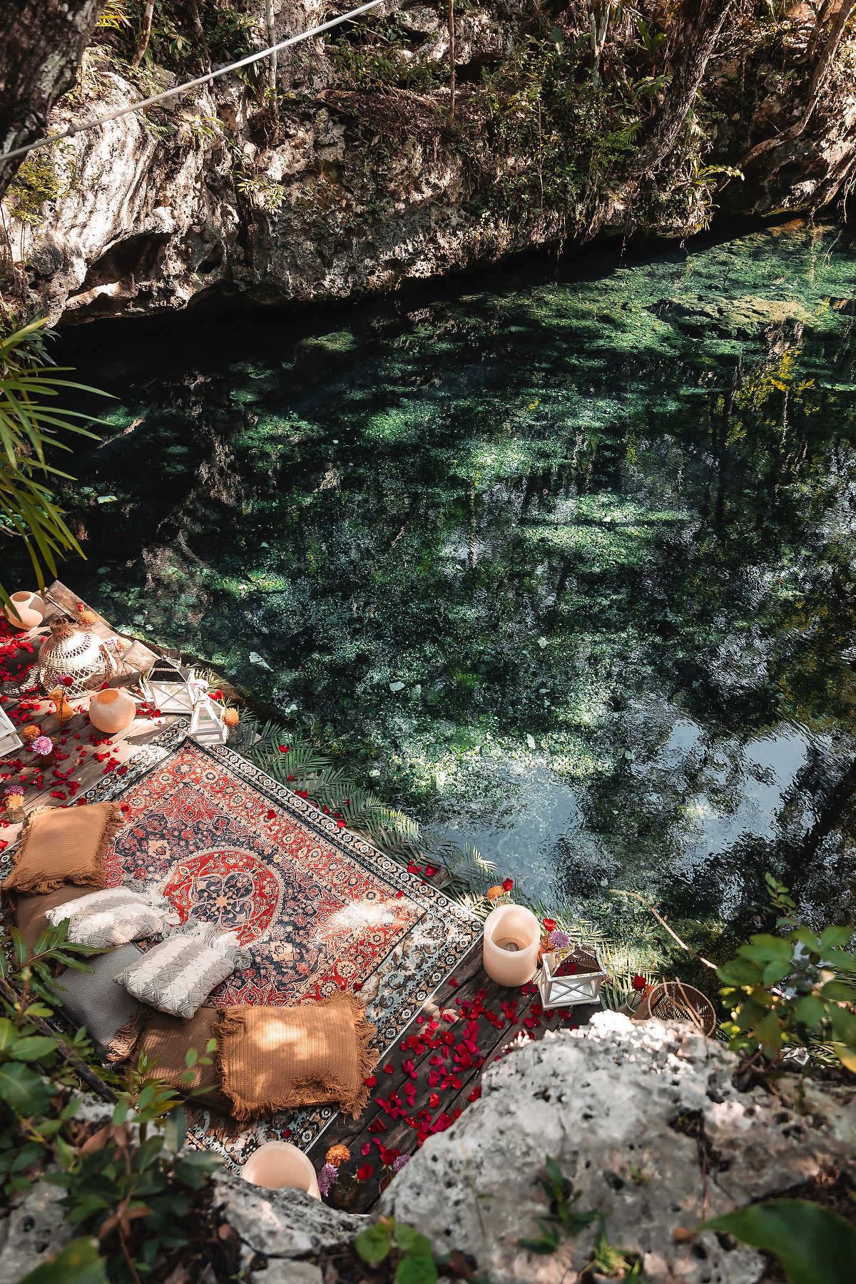 A red Persian rug laid out near crystal-clear turquoise waters of a natural cenote.