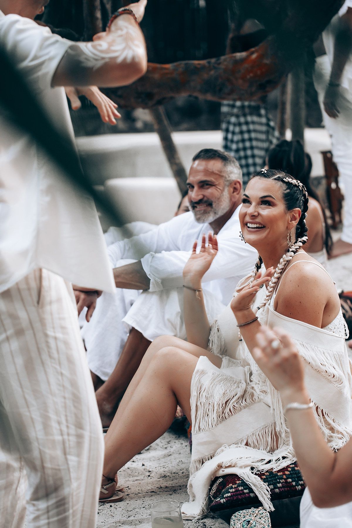 Group enjoying a festive gathering on the beach wearing white outfits.