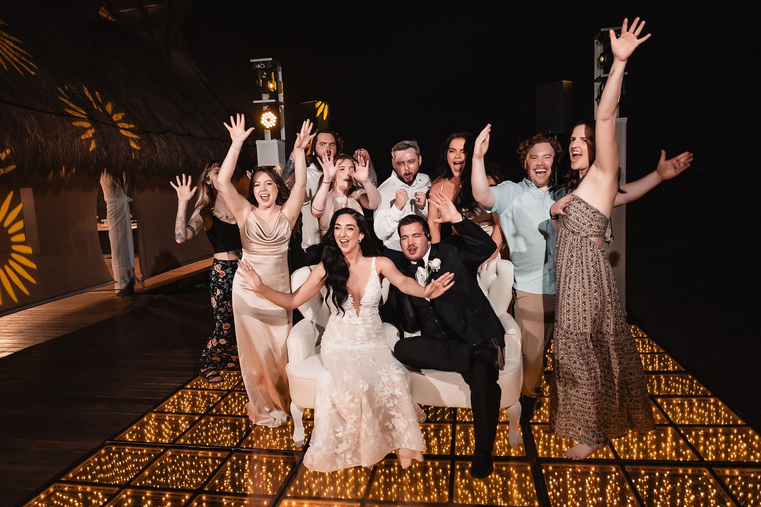 Wedding party celebrates with energetic dance moves under ambient lighting.