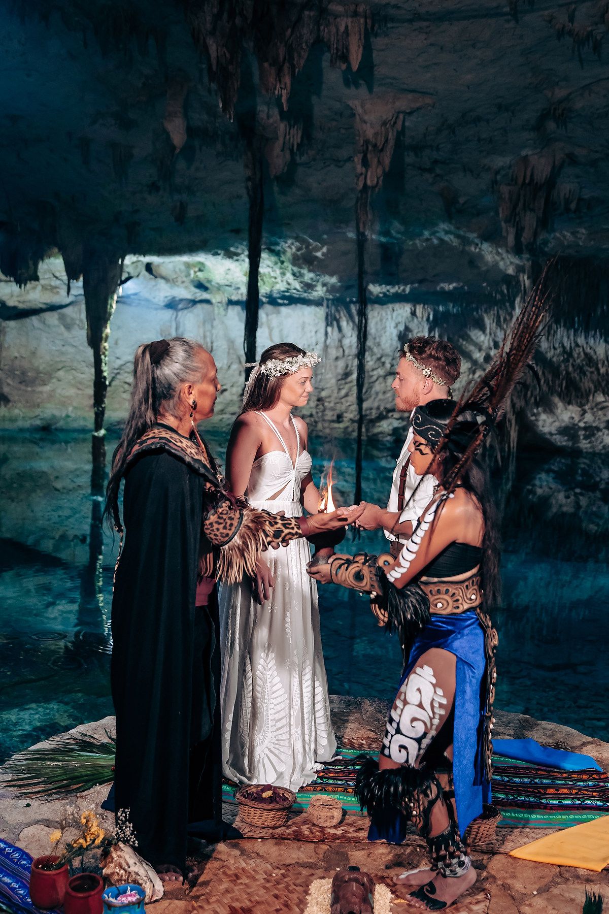 A wedding ceremony takes place in a mystical underground cave with turquoise water and stalactites visible in the background.