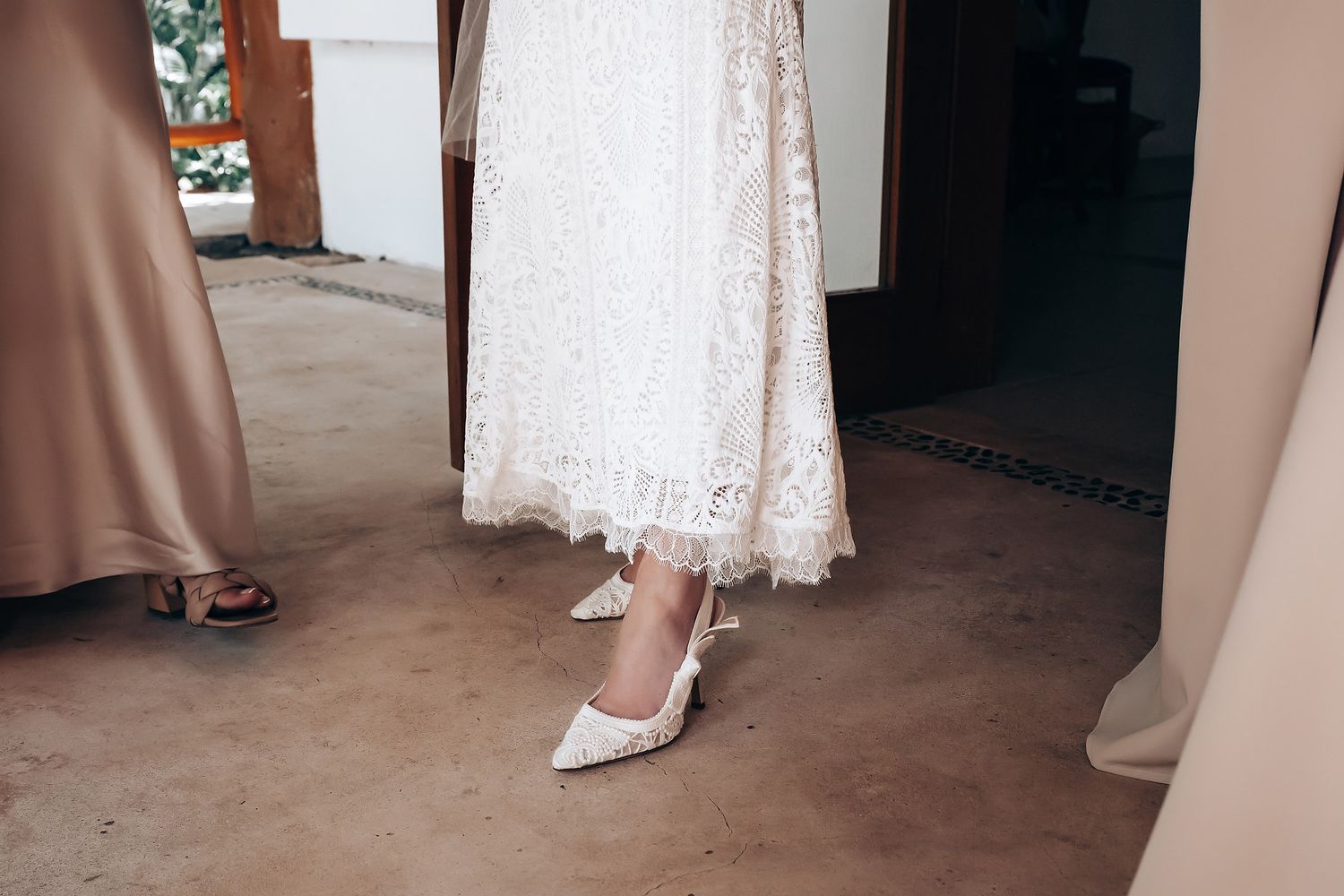 Close-up view of elegant bridal shoes with delicate lace details and soft pink undertones on a hardwood floor.