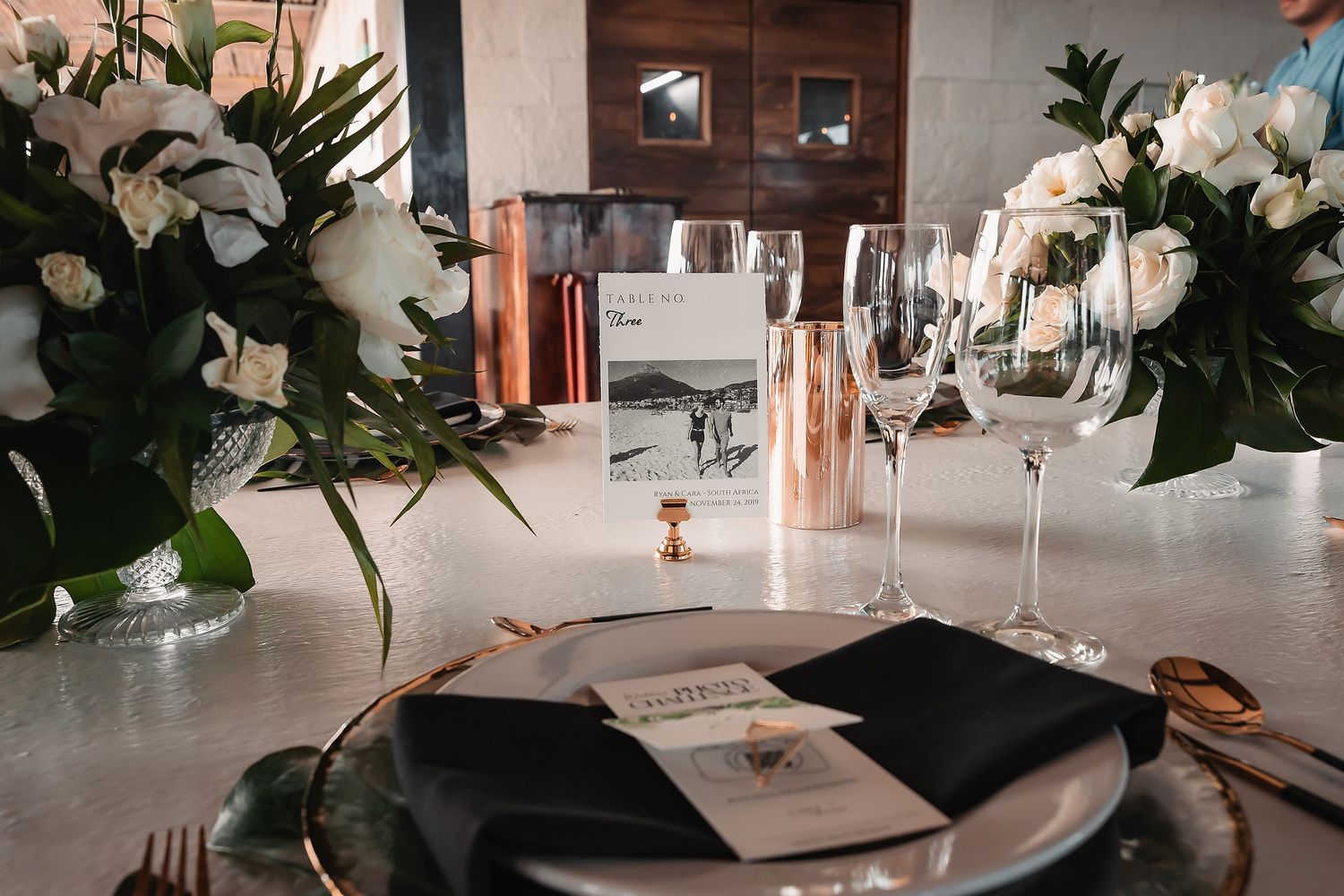 Elegant place settings with black plates and rose gold accents at wedding reception.