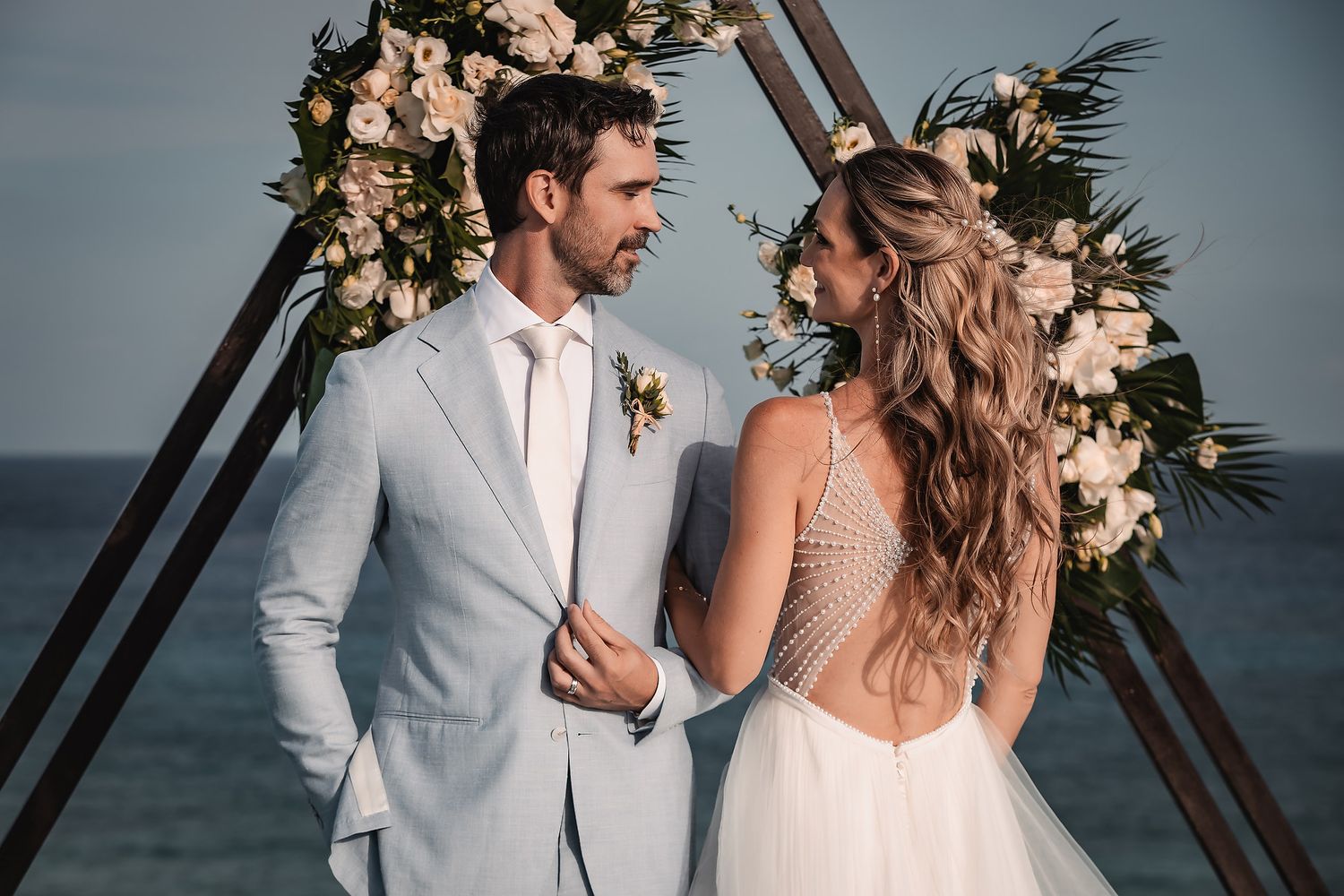 Elegant beach wedding ceremony with triangular floral arch and reflective platform.