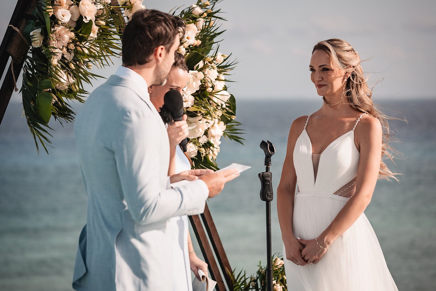 Emotional wedding ceremony moment during vow exchange with ocean and floral backdrop.