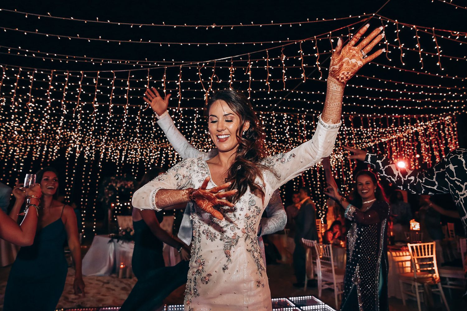 Wedding guests dancing and celebrating under twinkling string lights at an outdoor evening reception.