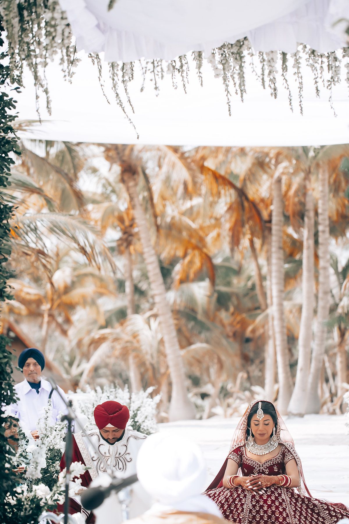 Intimate wedding ceremony moment captured under hanging floral decorations and palm trees.