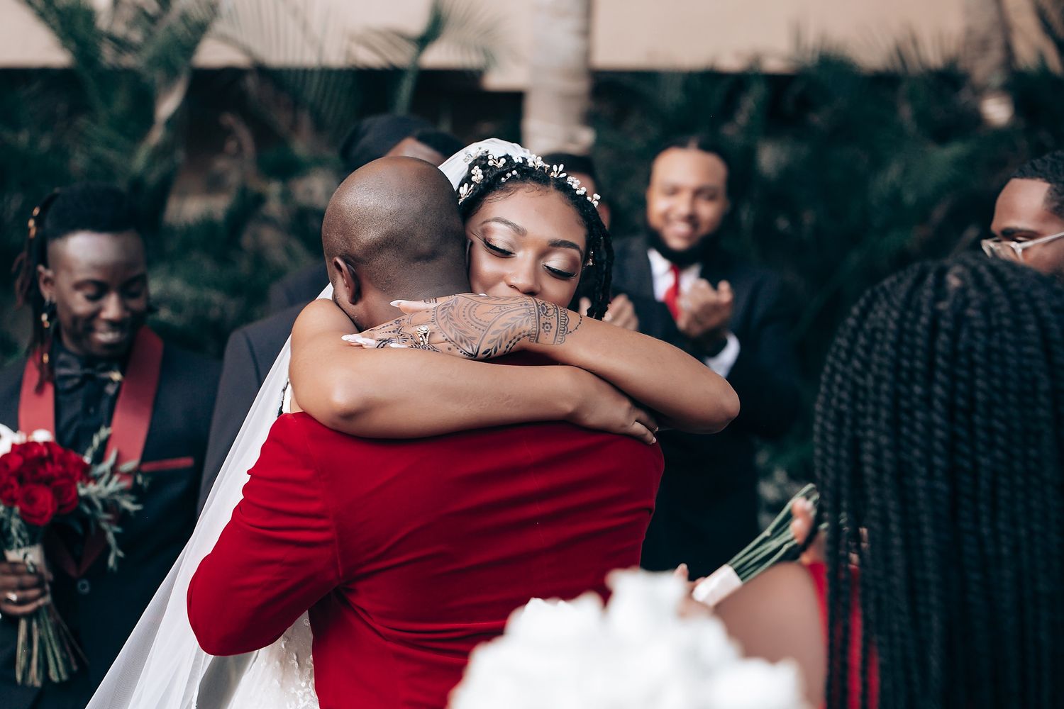 A joyful embrace between wedding couple in red and white attire during an outdoor celebration.