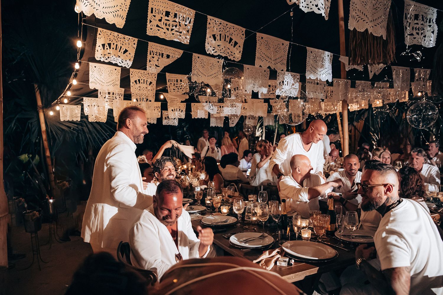 Crowded indoor venue with people in white attire celebrating under hanging paper decorations.
