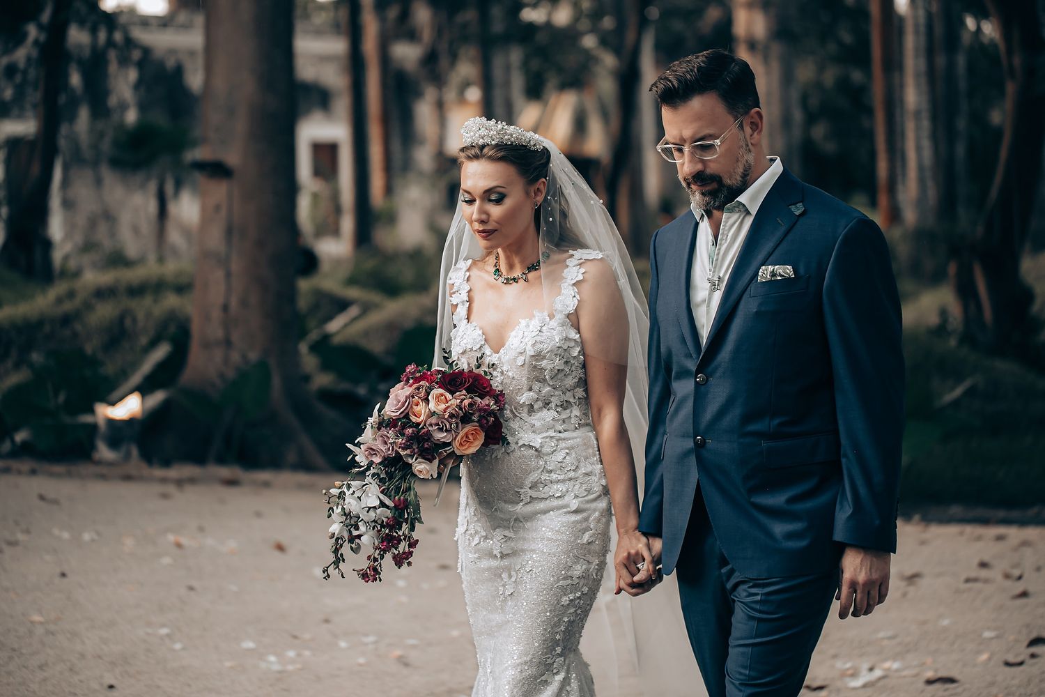 A bride and groom walk together on a stone path during their outdoor autumn wedding celebration.