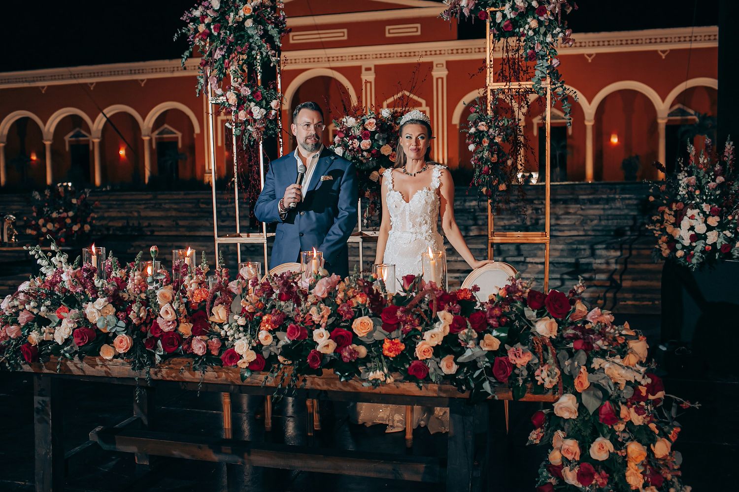 Wedding ceremony with floral arch decorations at a historic red brick building with guests seated outdoors.