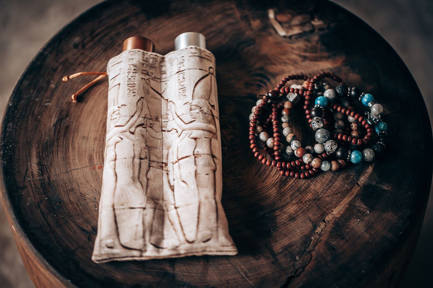 A collection of handmade jewelry and carved stone pieces arranged on a dark wooden surface with moody lighting.