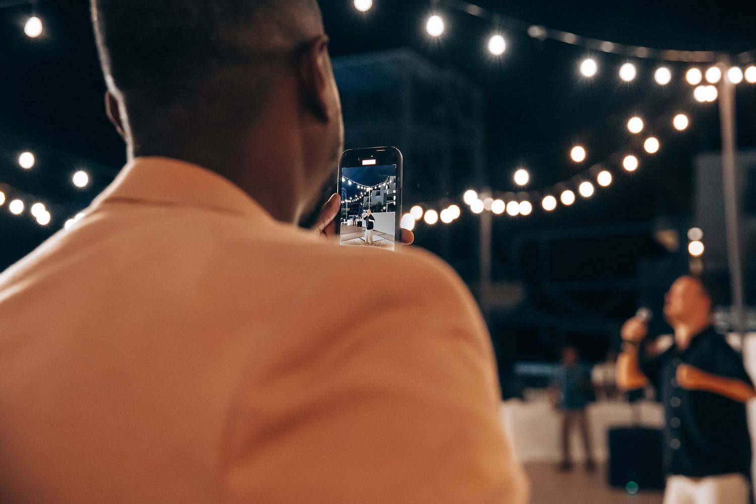 Warm string lights create bokeh effects against a dark night sky at an outdoor event.
