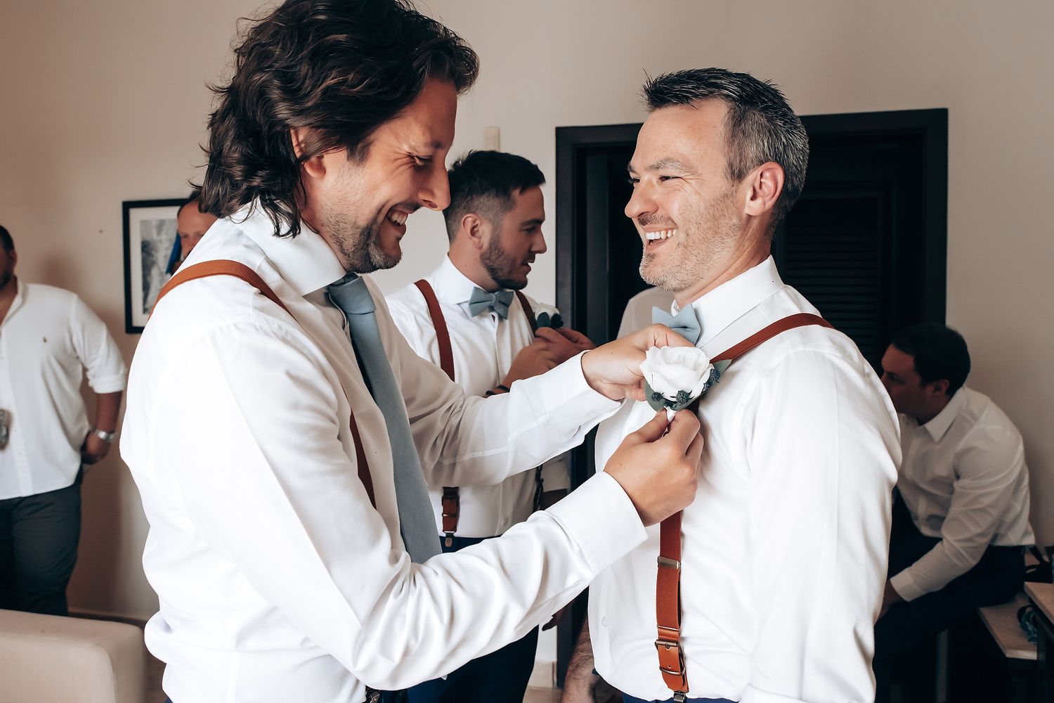 Groomsmen help each other prepare by adjusting ties and boutonnieres before a formal event.