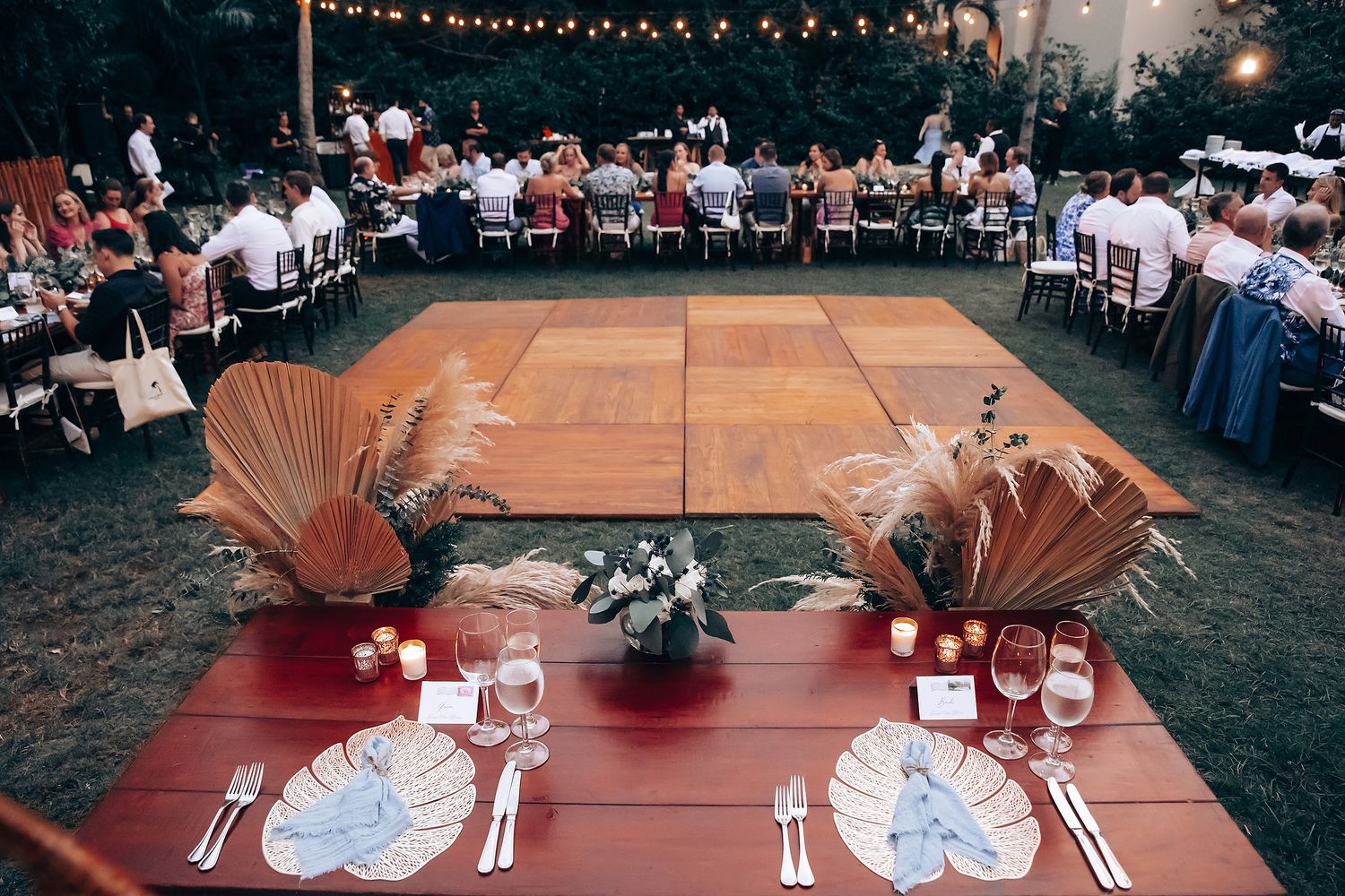 Elegant outdoor wedding reception setup with string lights and table settings at dusk.