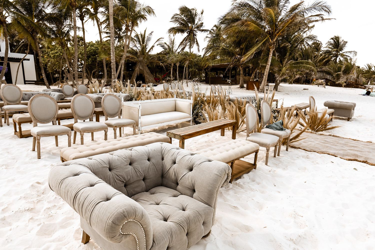 Elegant beach wedding reception setup with tufted lounge furniture on white sand.