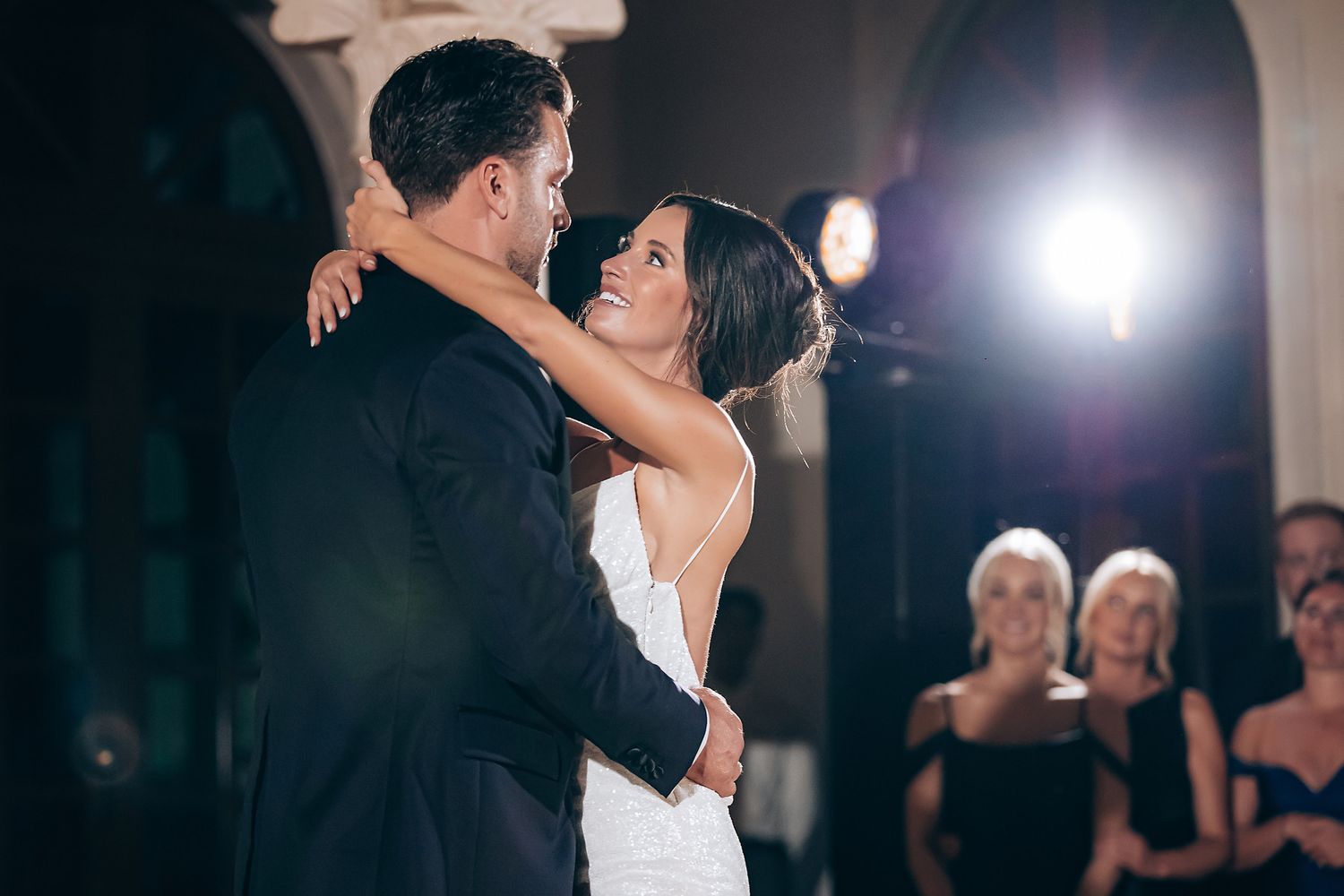 Newlyweds dancing together during their reception with dramatic lighting effects.