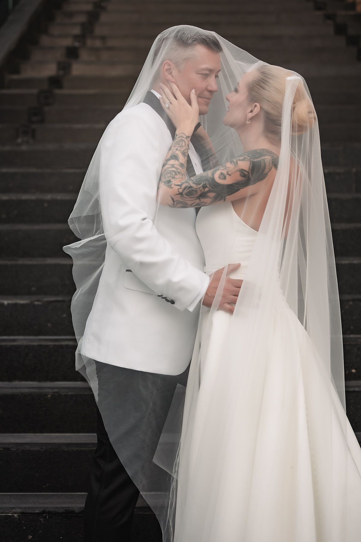 Romantic wedding moment captured on dark stairs with flowing white veil and dress details.