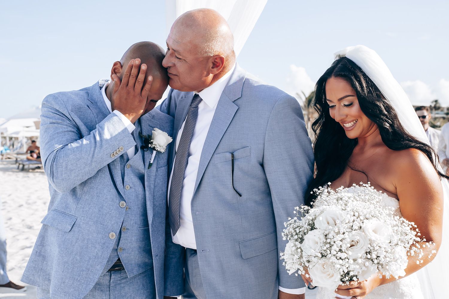 Wedding couple in light blue and white attire embracing during beach ceremony.