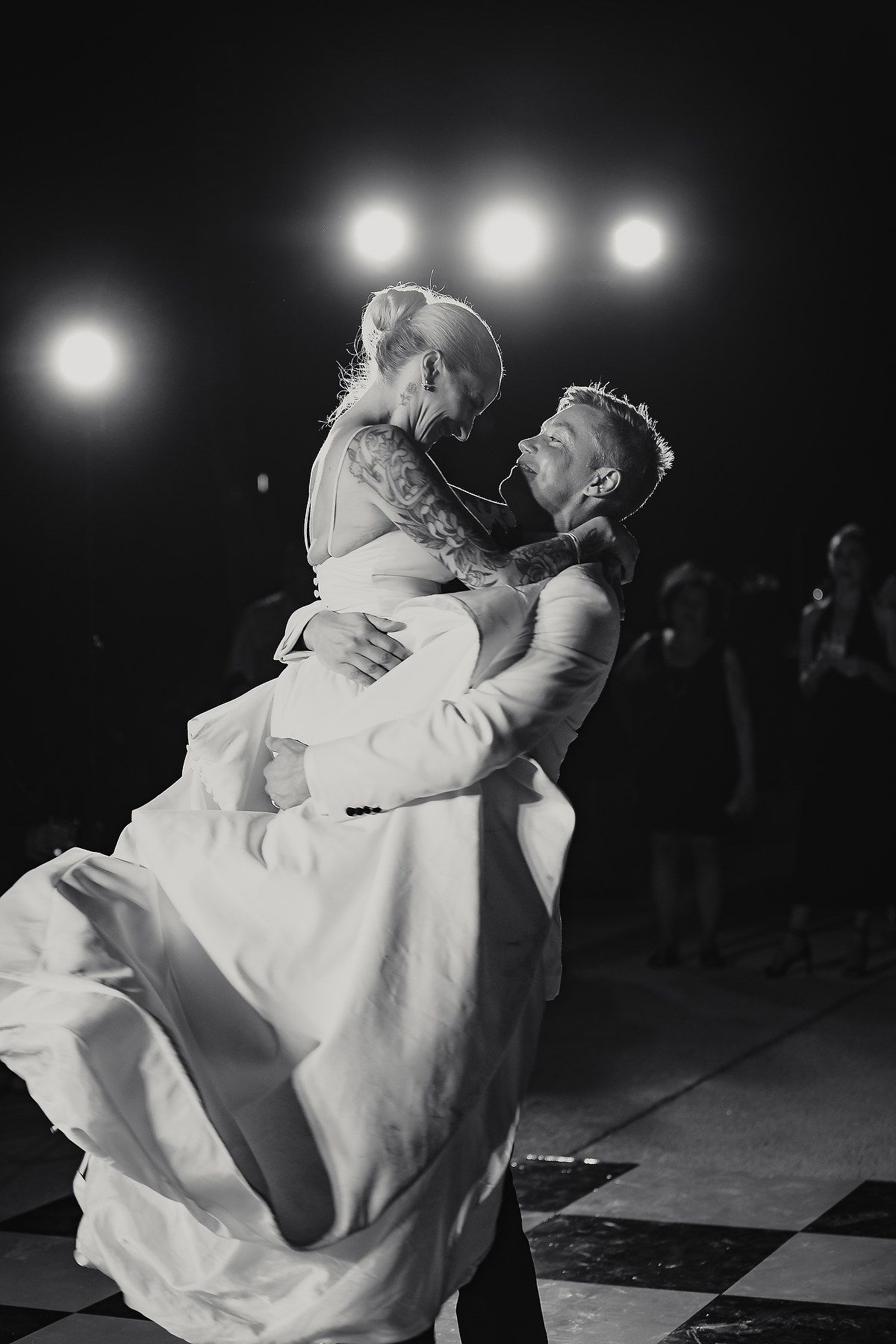 Black and white photo of newlyweds sharing first dance on checkered dance floor.