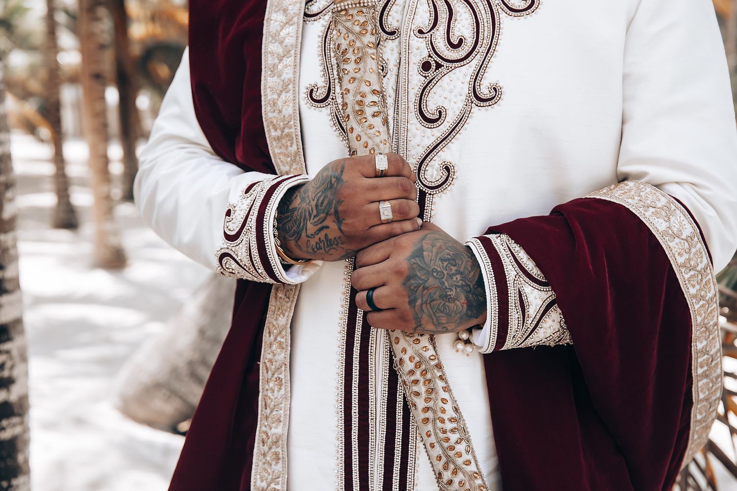 Traditional Indian wedding attire featuring intricate embroidery and burgundy accents in a tropical setting.