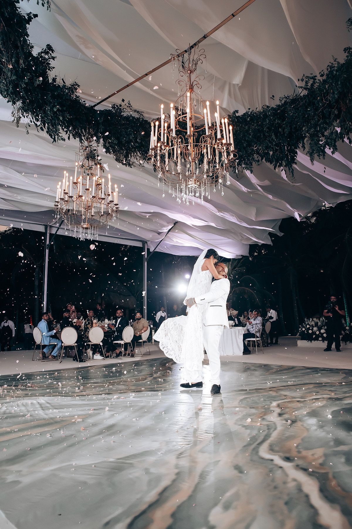Low angle view of couple dancing under crystal chandeliers with dramatic lighting effects.