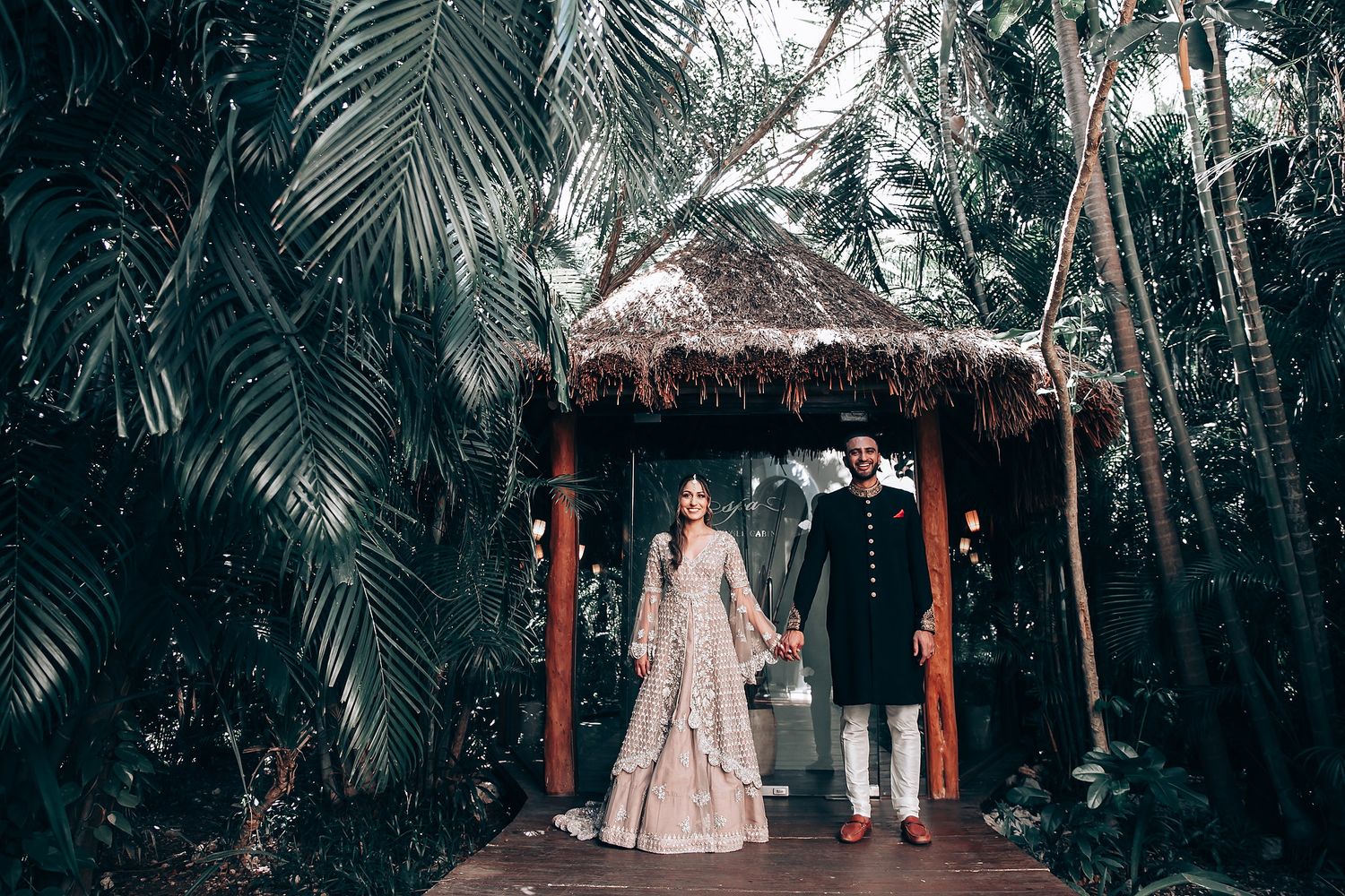 Wedding venue decorated with string lights and thatched roof in tropical garden setting.