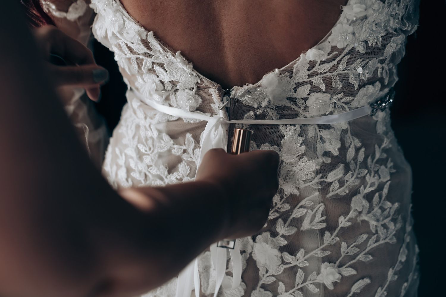 A close-up detail shot of an elegant white lace wedding dress with intricate floral patterns and delicate beading.