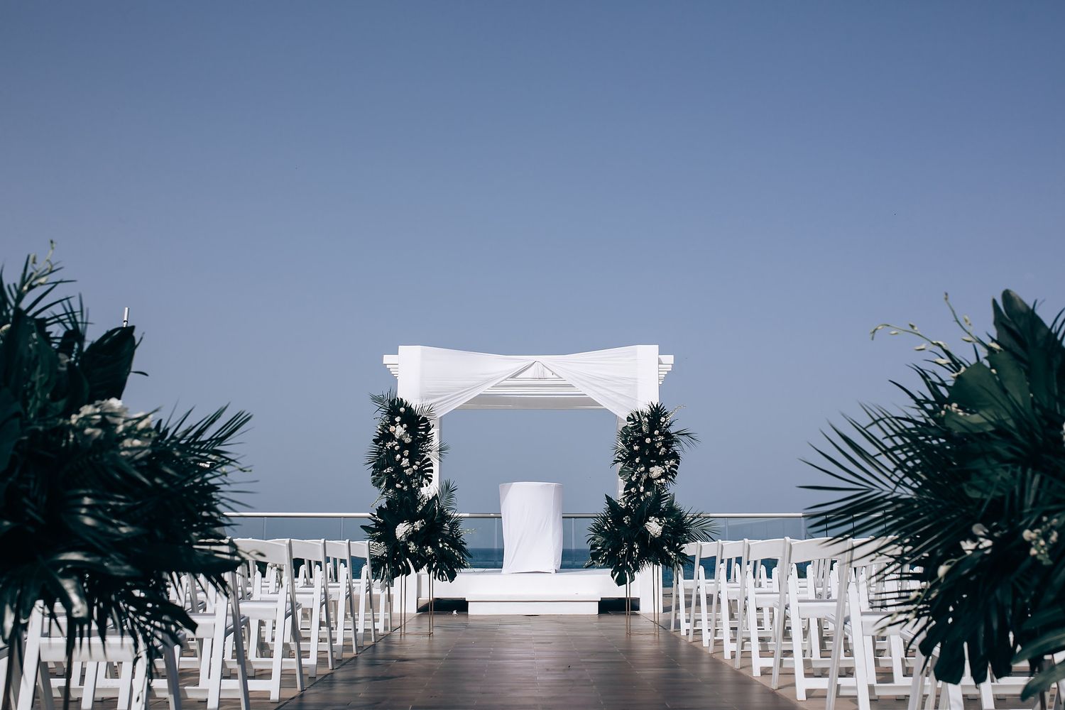Panoramic view of a white wedding ceremony setup with palm trees and ocean backdrop.