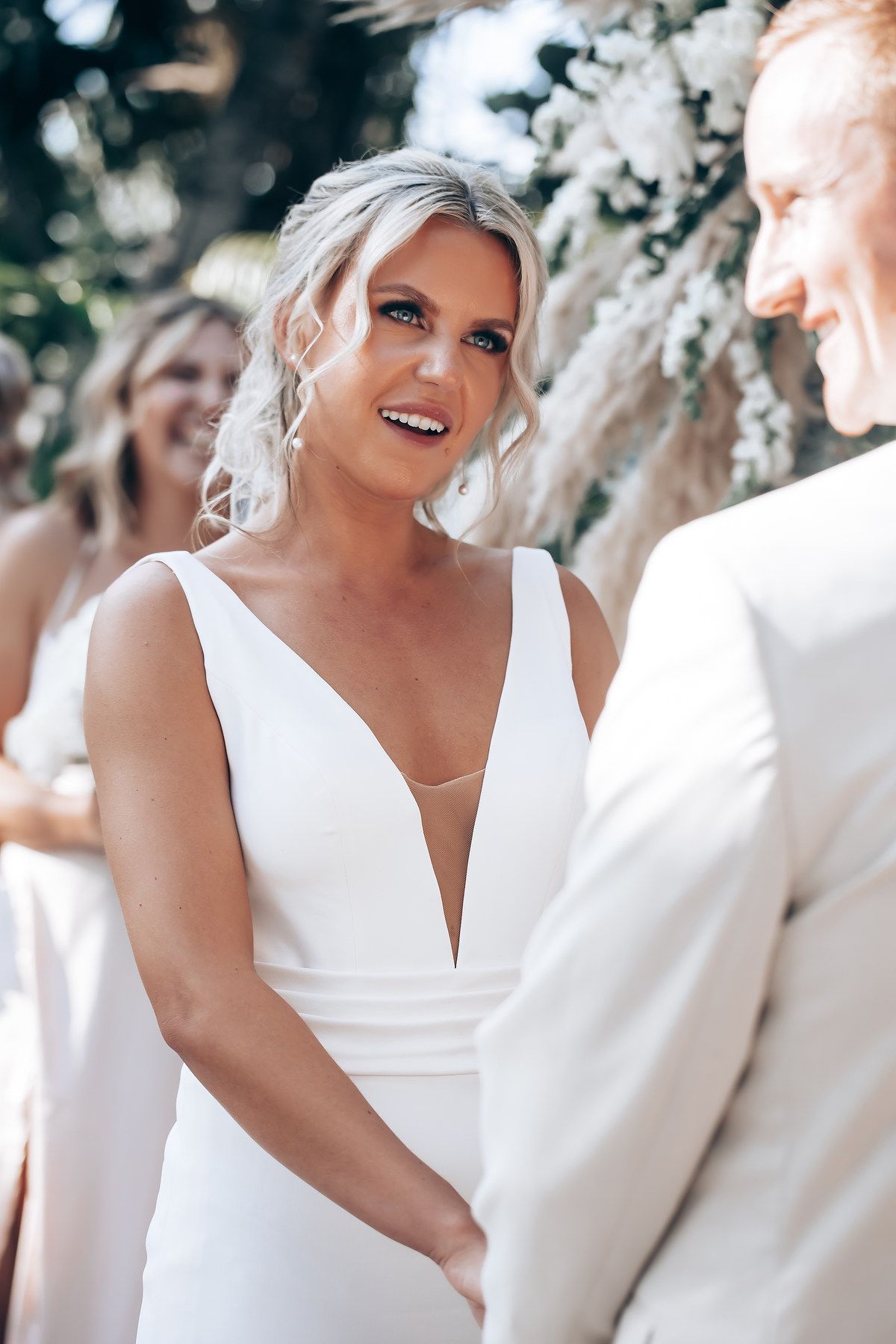 Wedding party members in white attire sharing joyful moments during an outdoor celebration.