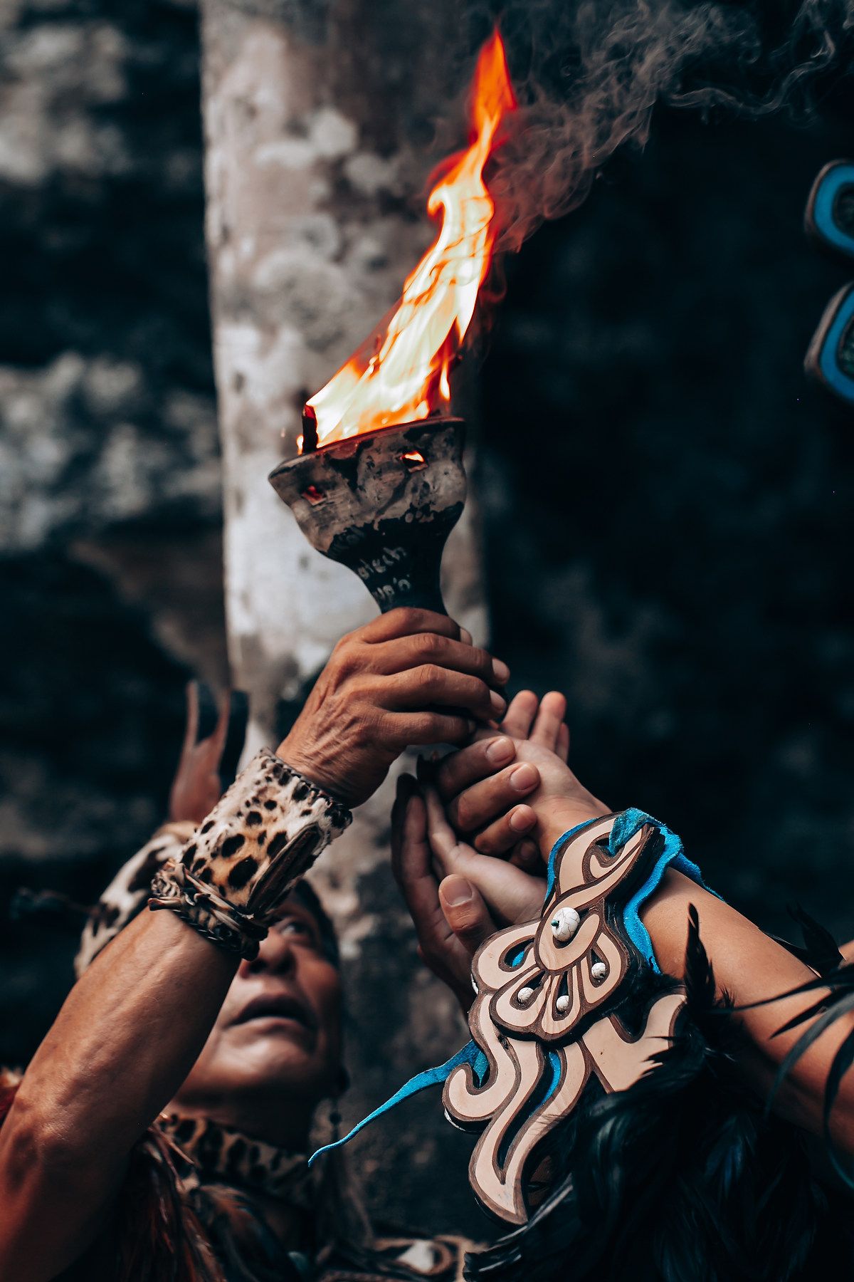 Hands holding a burning ceremonial torch with leopard print and blue Mayan costume details visible below.